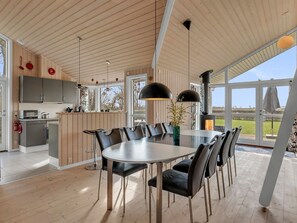 Eine moderne Küche mit Holzschränken, ein Essbereich mit einem runden Tisch und Stühlen sowie große Fenster mit Blick ins Freie.