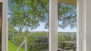 Un balcó de fusta amb barana metàl·lica, vista despejada d'arbres i vegetació, i un indici d'un edifici al fons.