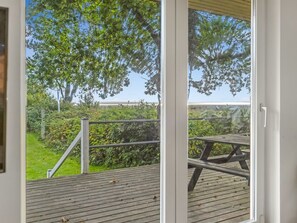Eine Holzterrasse mit Metallgeländer, freie Aussicht auf Bäume und Grünflächen, und ein Blick auf ein Gebäude im Hintergrund.
