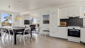 Una cuina moderna amb armaris blancs, una zona de menjador amb taula i cadires, i un gran finestral que aporta llum natural.