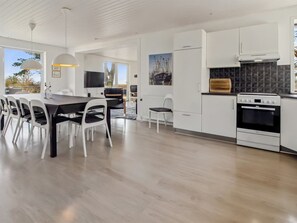 Eine moderne Küche mit weißen Schränken, ein Essbereich mit Tisch und Stühlen sowie ein großes Fenster, das für natürliches Licht sorgt.