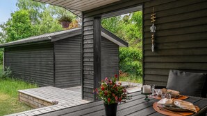 En träveranda med ett bord dukat för middag, ett litet förråd i bakgrunden och en krukväxt på bordet.