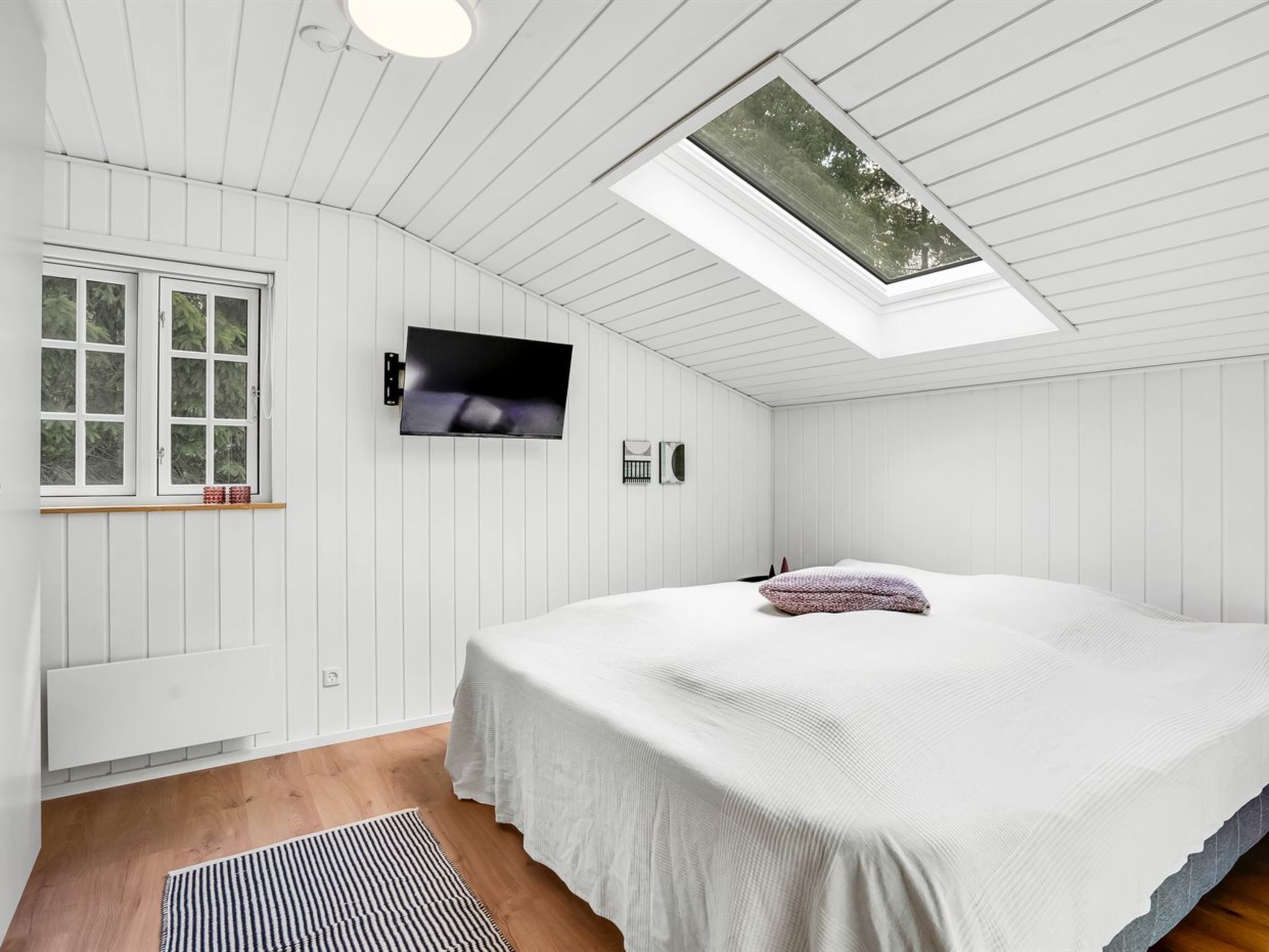 A bedroom with a skylight, a bed, a TV, and a window.