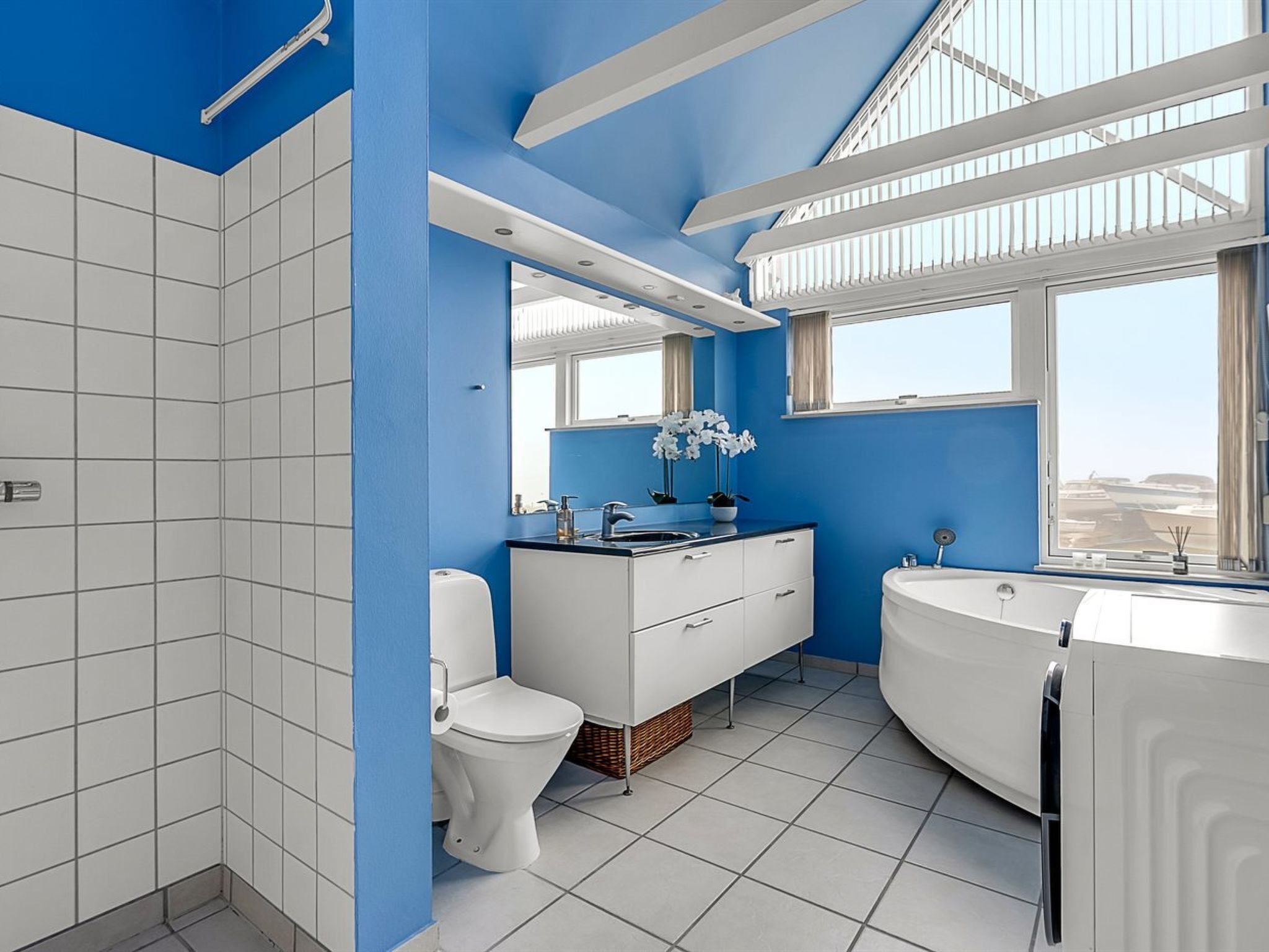 Un bany modern amb una paret d'accent blau, un vàter blanc, un lavabo, una banyera i una finestra amb vistes.