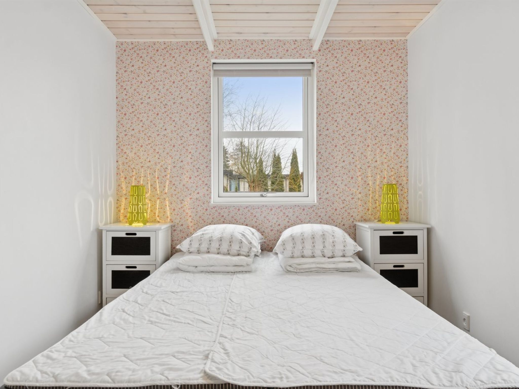 A bedroom with a bed, two bedside tables, a window, and a view of trees outside.