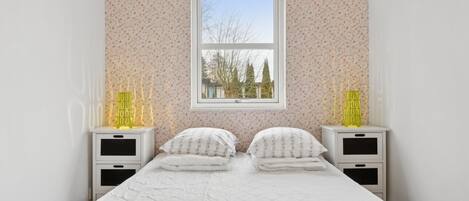 A bedroom with a bed, two bedside tables, a window, and a view of trees outside.