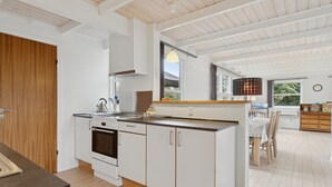 A modern kitchen with white cabinetry, a built-in oven, and a dining area with a wooden table and chairs. - "Gittel" - 200m from the sea by Interhome (Rønne)