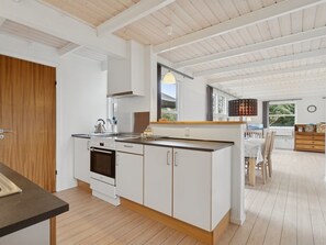A modern kitchen with white cabinetry, a built-in oven, and a dining area with a wooden table and chairs. - "Gittel" - 200m from the sea by Interhome (Rønne)