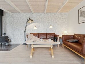 A cozy living room with a round coffee table, a brown leather sofa, a black fireplace, and a patterned wall. - "Gittel" - 200m from the sea by Interhome (Rønne)
