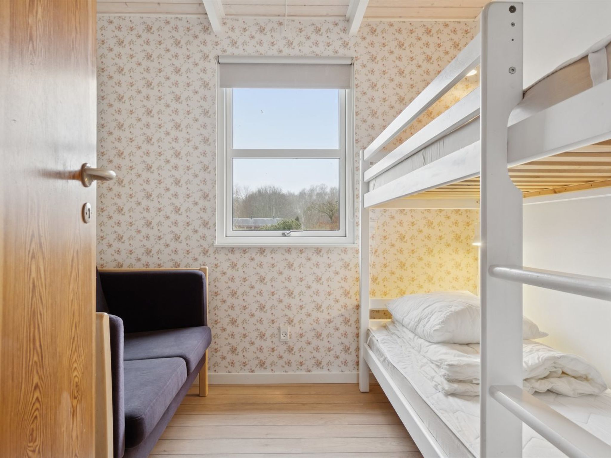 A room with a bunk bed, a sofa, a window, and floral wallpaper.