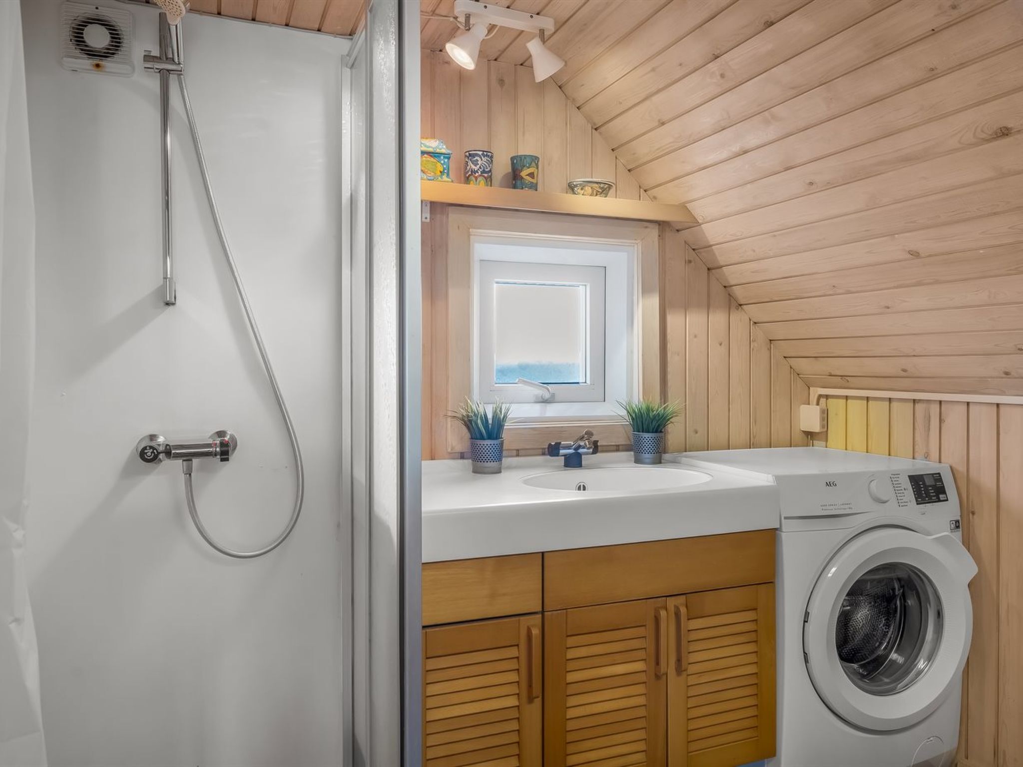 Ein kleines, modernes Badezimmer mit Waschmaschine, Dusche und einem Fenster über dem Waschbecken.
