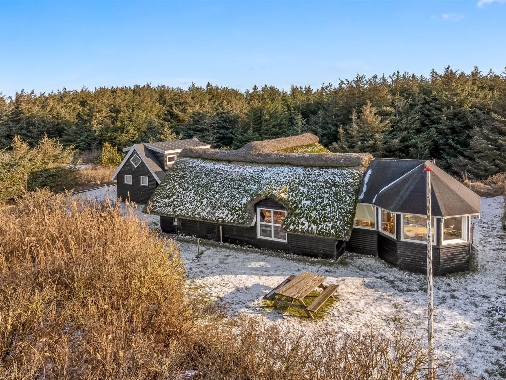 Une maison traditionnelle en bois, avec un toit de chaume, entourée d’un paysage enneigé et d’une forêt dense.