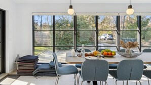 A modern dining area with a view of the outdoors, featuring a table set with fruits, a candle, and a vase with dried flowers.