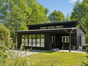 Ein modernes Haus mit großen Fenstern, einer überdachten Veranda und einer kleinen Außenküche.