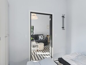 Ein modernes Zimmer mit einem Bett, einer Couch, einem kleinen Tisch und einem Stuhl. Eine Tür führt in einen weiteren Raum.