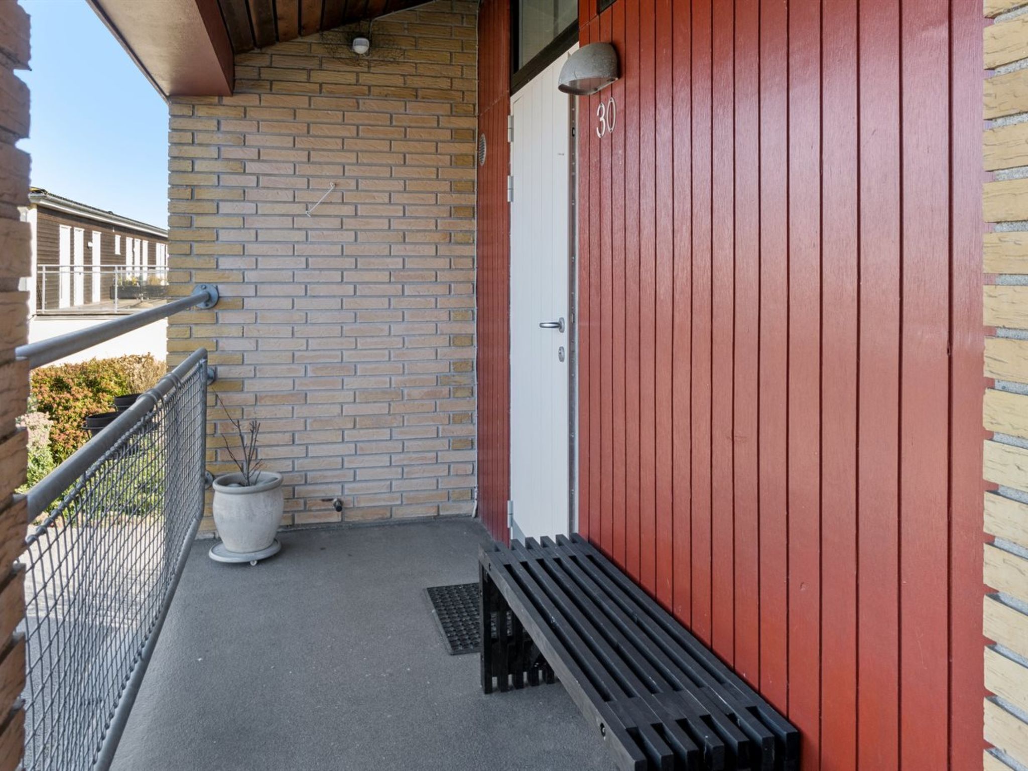 A balcony with a metal railing, a potted plant, and a red door.