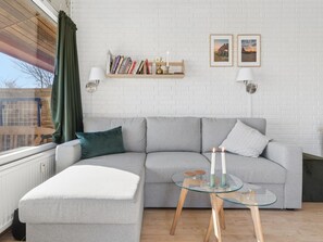 Ein modernes Wohnzimmer mit grauem Sofa, einem Glastisch und einem Bücherregal mit Büchern und Dekoration.