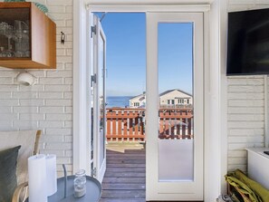 A room with a white brick wall, a wooden table with candles, a TV, and a door leading to a balcony with a view of houses and a fence. - "Amilia" - 100m from the sea by Interhome (Allinge)