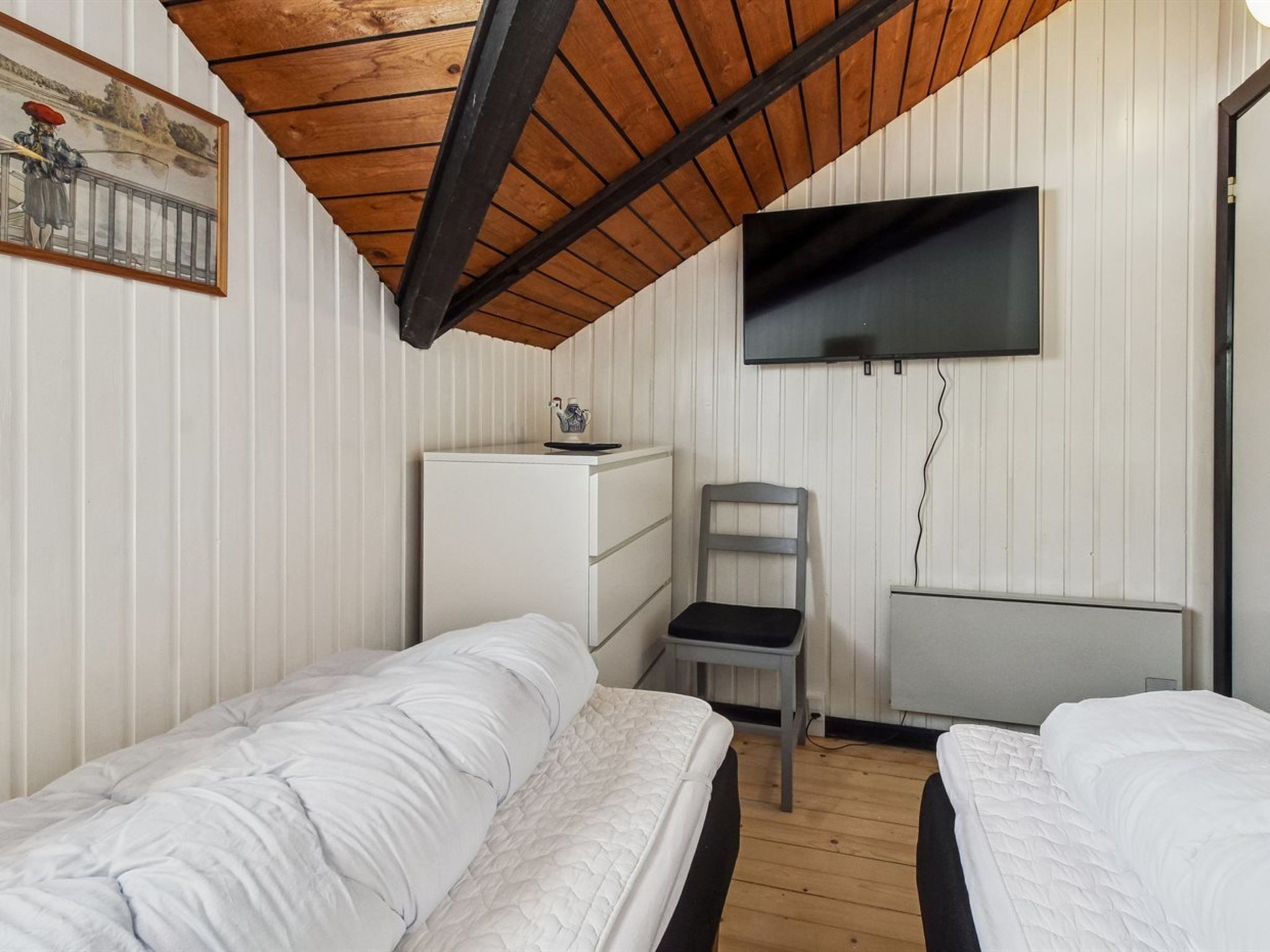 A room with two beds, a desk, a chair, a television, and a radiator.