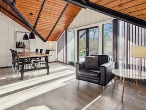 A spacious room with a high ceiling, a dining area with a wooden table and chairs, a leather sofa, and large windows offering a view of the outdoors. - "Sölvy" - 30km from the sea by Interhome (Toftlund)