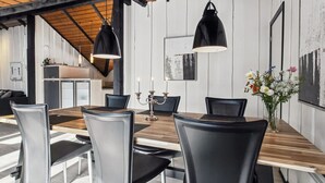 Ein Essbereich mit einem Holztisch, schwarzen Stühlen, Pendelleuchten und einem Blumenstrauß.