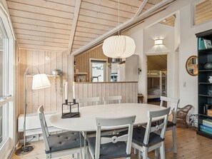 Een eetruimte met een ronde tafel, witte stoelen, een hanglamp en een moderne keuken op de achtergrond.