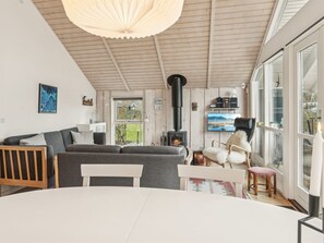Een gezellige woonkamer met een bank, een tafel, een open haard en grote ramen.