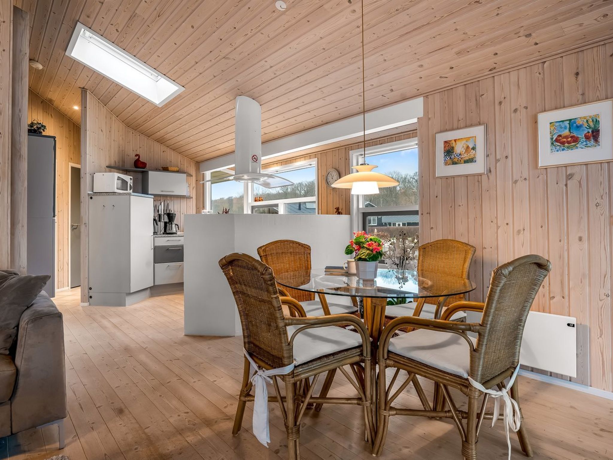 A modern kitchen with white cabinets, a central island, and a dining area with wicker chairs and a glass table.