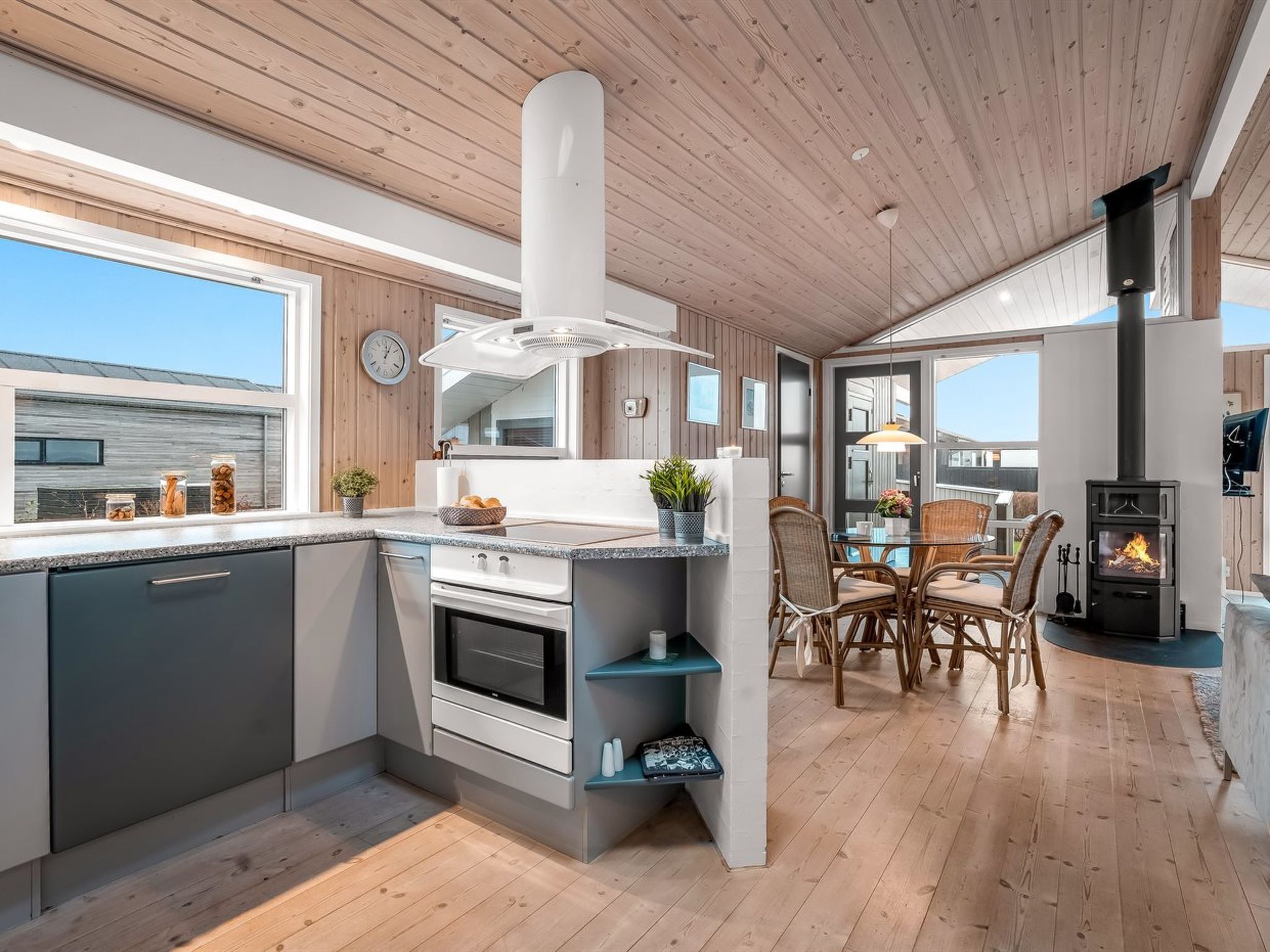 Et moderne køkken med indbygget komfur, træloft og et spiseområde med fletstole.