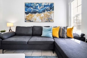 Un soggiorno moderno con un divano modulare grigio, una lampada da terra e un grande quadro astratto appeso al muro.