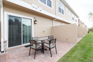 Une terrasse avec une table et des chaises, une porte-fenêtre coulissante et un mur extérieur de couleur beige.