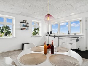 A modern kitchen with white cabinets, a dining table with placemats, and a hanging pendant light. - "Carola" - 1km from the sea by Interhome (Svaneke)