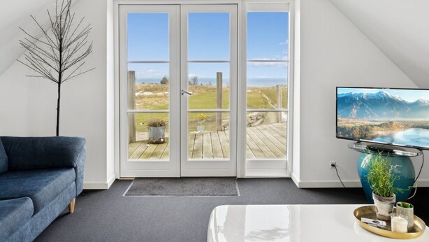 Ein modernes Wohnzimmer mit großem Fenster, Fernseher und einem blauen Sofa.