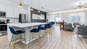 Une cuisine moderne avec des meubles blancs, un îlot central doté de tabourets et un coin repas avec une table et des chaises.