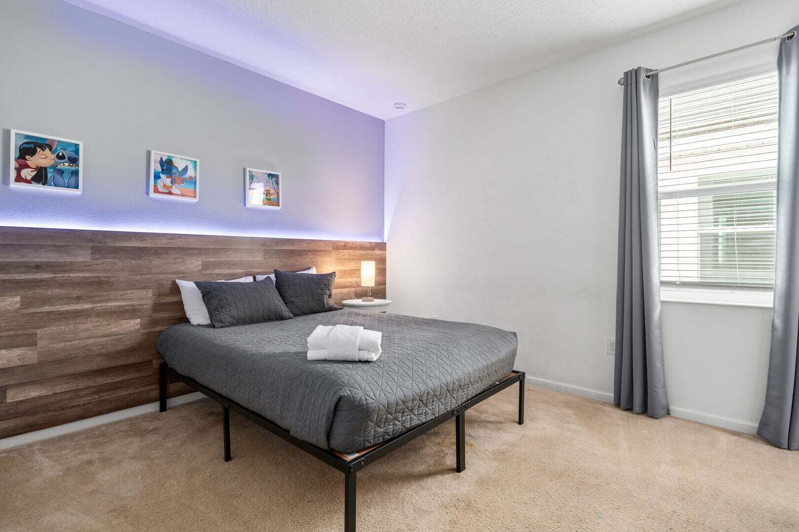 Un dormitorio moderno con cabecera de madera, cama con ropa de cama gris, una lámpara de noche y tres cuadros enmarcados en la pared.
