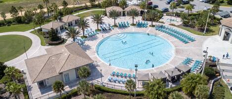 An aerial view of a residential area with a central swimming pool surrounded by lounge chairs and palm trees.