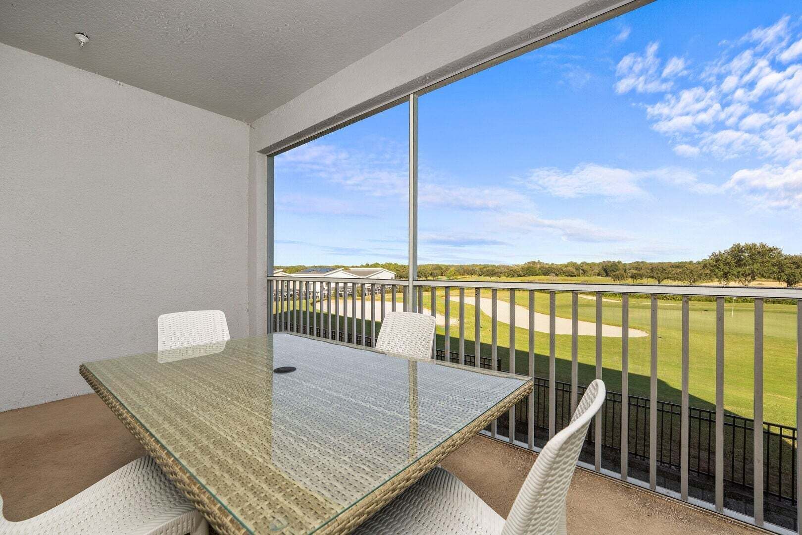Een balkon met een tafel en stoelen, met uitzicht op een golfbaan.
