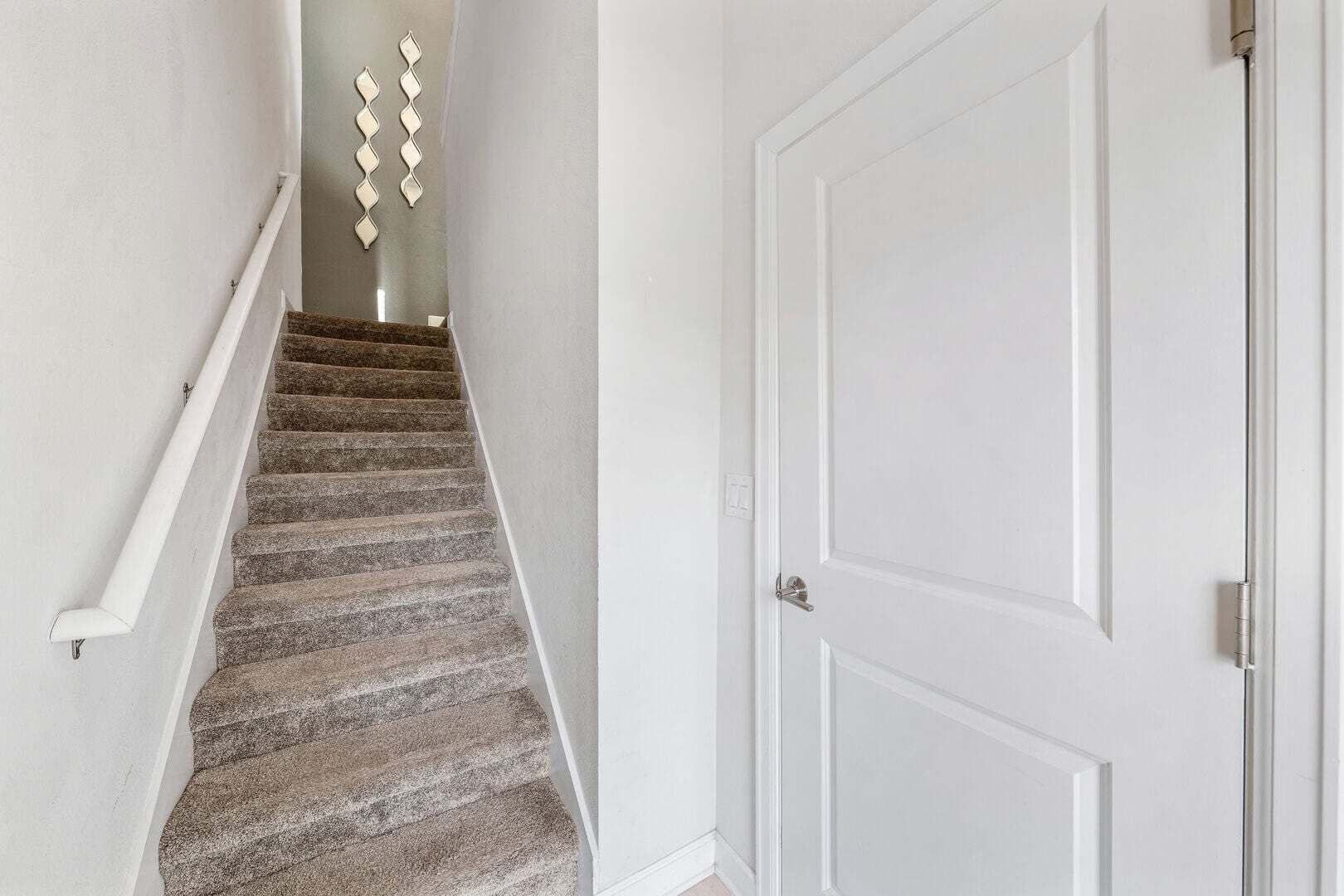 Un escalier recouvert d’une moquette à motifs, une porte blanche et un luminaire fixé au mur.