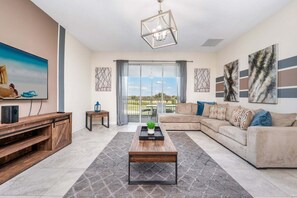 A living room with a sofa, coffee table, TV, and artwork. - Beautiful Golf Course View Townhome! (Davenport)