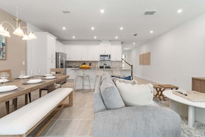 Uma cozinha moderna com armários brancos, uma ilha central e um espaço de refeições com um banco e mesa para quatro pessoas.