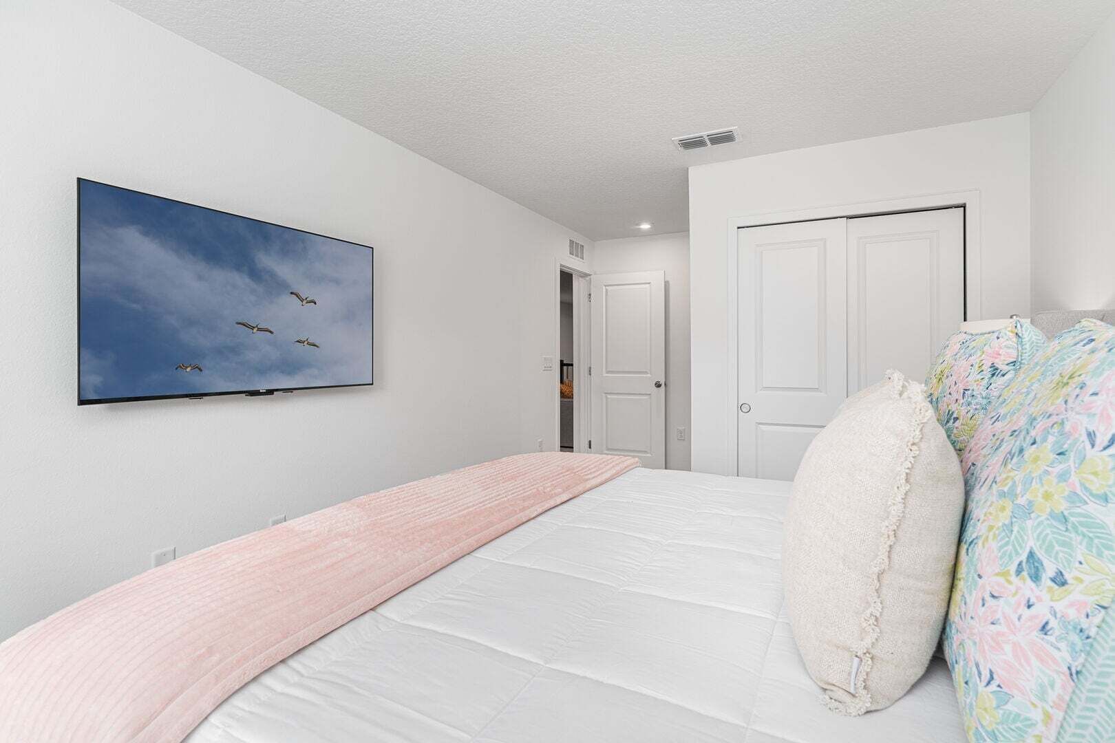 A bedroom with a bed, a wall-mounted TV, and a door.