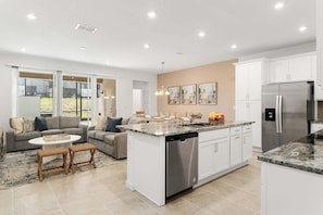 A modern kitchen with a central island, stainless steel appliances, and a dining area with a sofa and coffee table. - Bright and Comfy Villa Private Pool (Kissimmee)