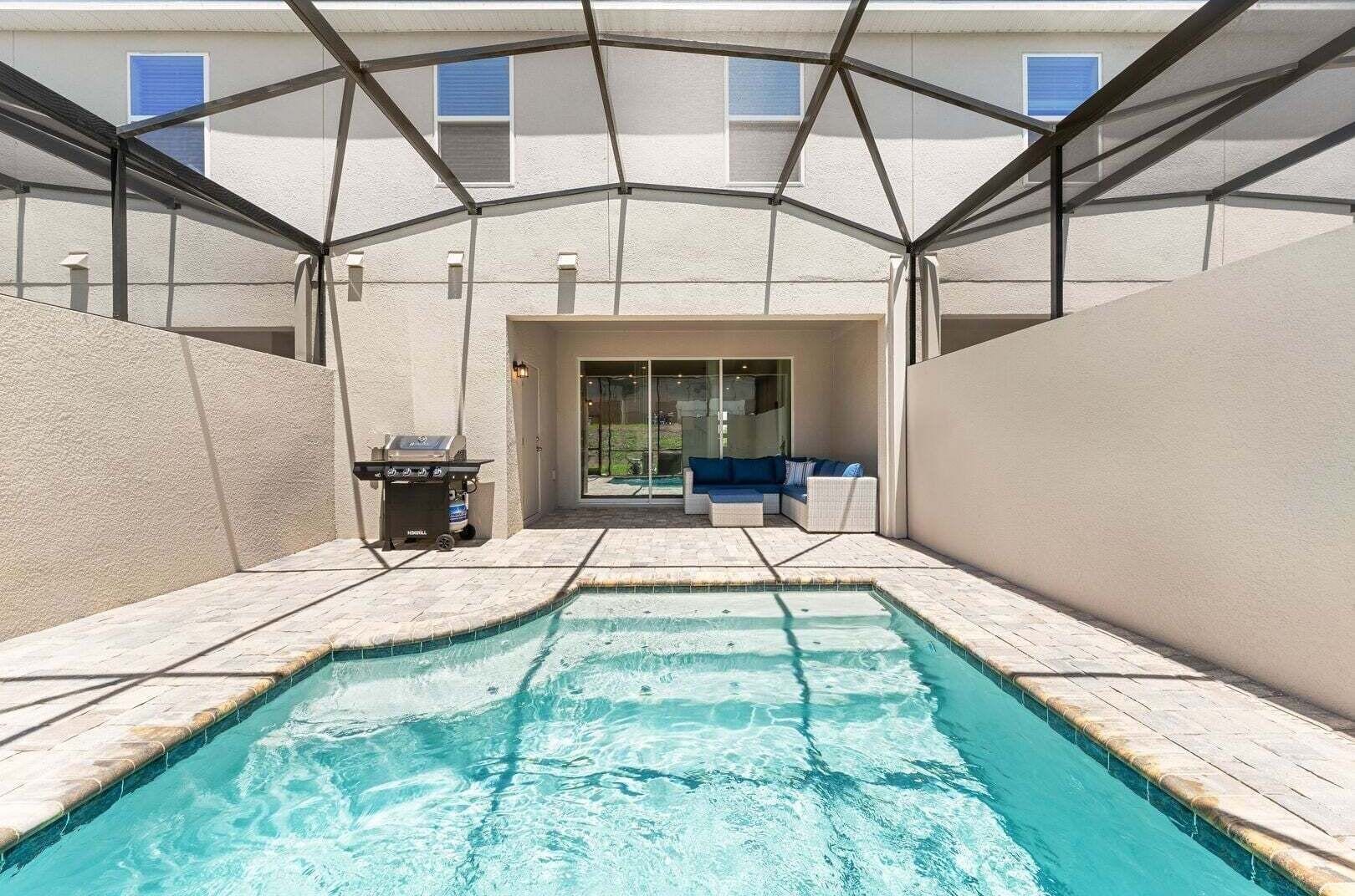 A swimming pool with a covered patio area, a grill, and a seating area with a view of the house.
