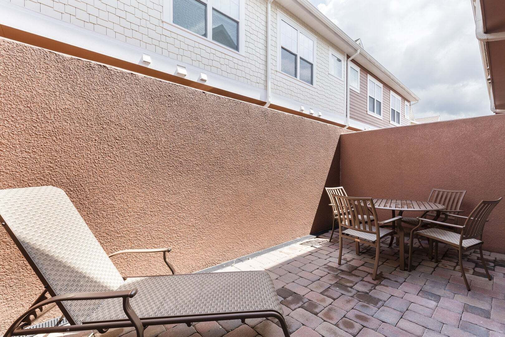 Eine Terrasse mit strukturierter Wand, einer Liege und einem Tisch mit Stühlen.