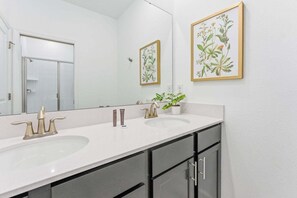 A bathroom with two sinks, a large mirror, and framed botanical prints on the wall. - Champions Gate Retreat: Private Pool & Top Resort (Davenport)