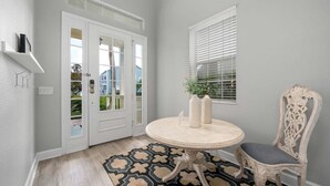 Une pièce avec une table ronde, deux vases, une chaise, un tapis à motifs, une porte blanche et une fenêtre avec des stores.