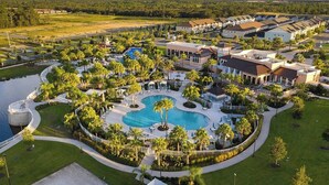 Ett flygbildsbild av ett semesterområde med en central pool, flera byggnader och omgivande grönska.