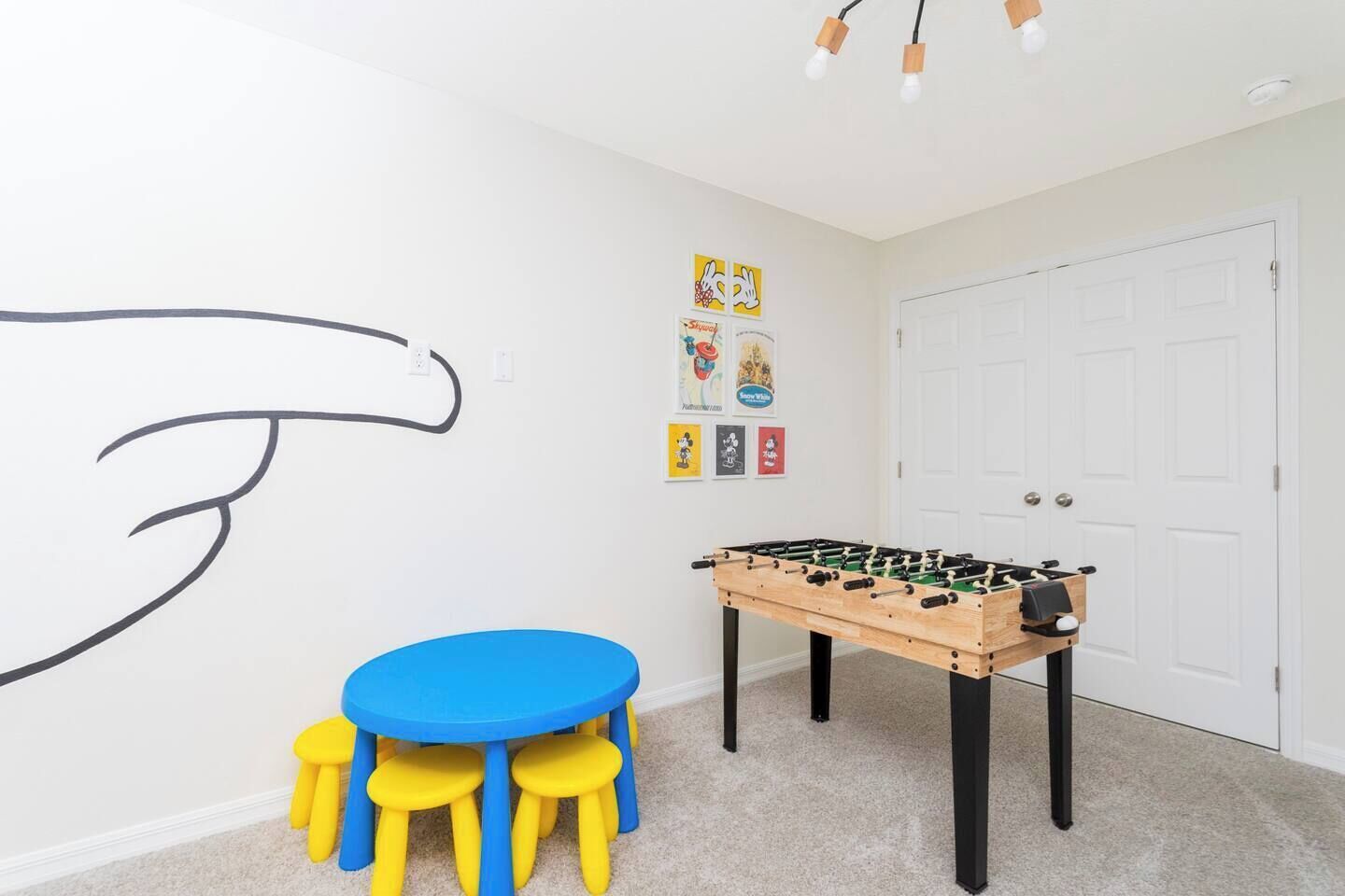 A room with a foosball table, a blue table, and yellow stools.