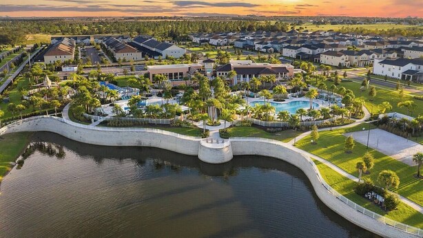 Ett flygbildsbild av ett bostadsområde med en central pool, omgiven av hus och grönska.