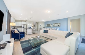 A modern living room with a sofa, a glass coffee table, and a blue chair. - Bright Big Home w/ Pool, Game Room & Resort Access (Kissimmee)
